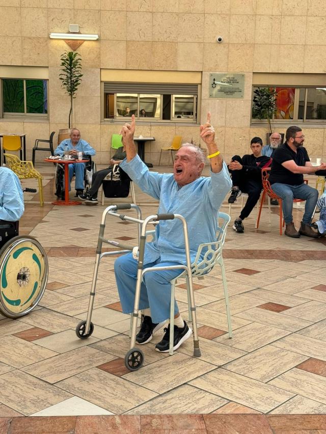 Old man in a wheelchair raising his hands in joy as he sings with the cantors while in the hospital atrium