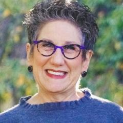 Woman with short spiky hair and purple glasses smiling at the camera