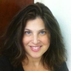 Smiling woman with long dark wavy hair. Wearing a black shirt.