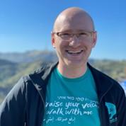 Bald man, smiling, wearing glasses and blue t-shirt